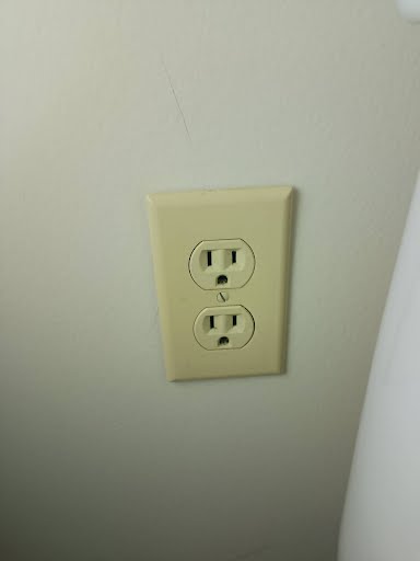 Completed wall outlet with ivory cover plate mounted neatly near the toilet