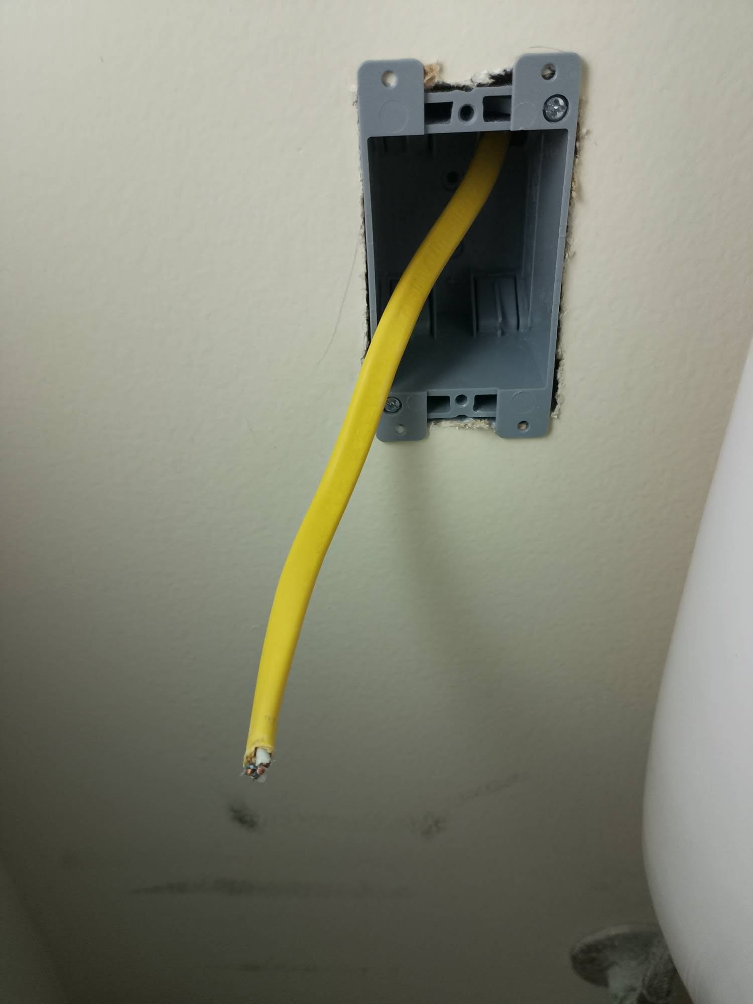 Blue plastic old work electrical box mounted in drywall cutout with wire pulled through